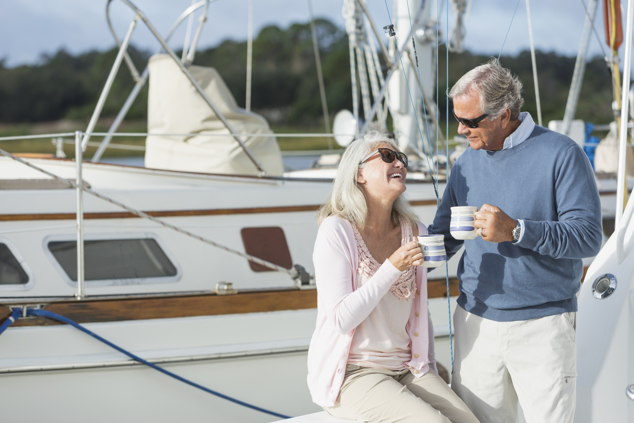 A happy, retired couple drinking coffee and conversing on their luxury boat at a marina.