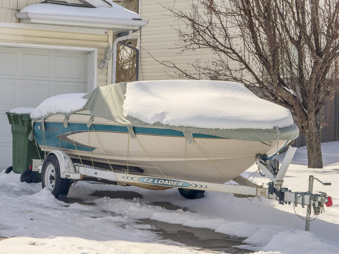 Calgary, Alberta, Canada. Mar 8, 2024. A boat sitting in front of a house garage, covered in snow during the winter.