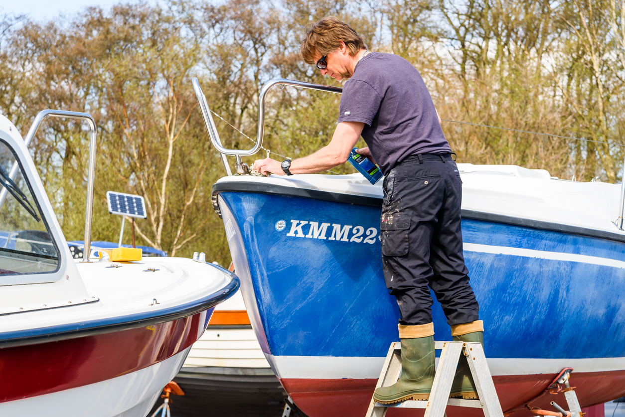 Raa harbor, Helsingborg, Sweden - April 29, 2018: Documentary of everyday life and place. Person standing on stepladder while waxing a boat in the marina.