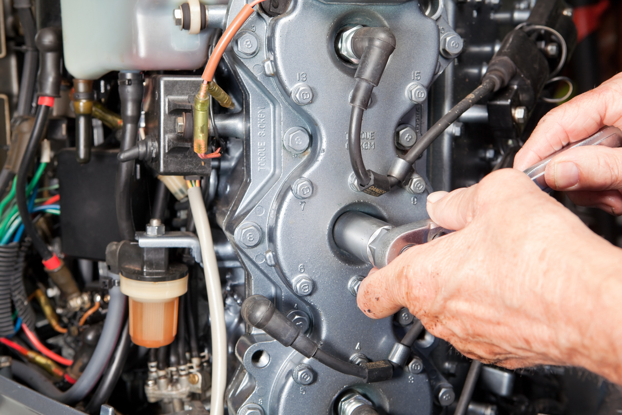 "A mechanic, with greasy hands, is using a socket wrench to install or remove a spark plug from a cylinder head on a outboard marine engine. This is a modern 6-cylinder, 200 hp motor with some dust and visible signs of wear."