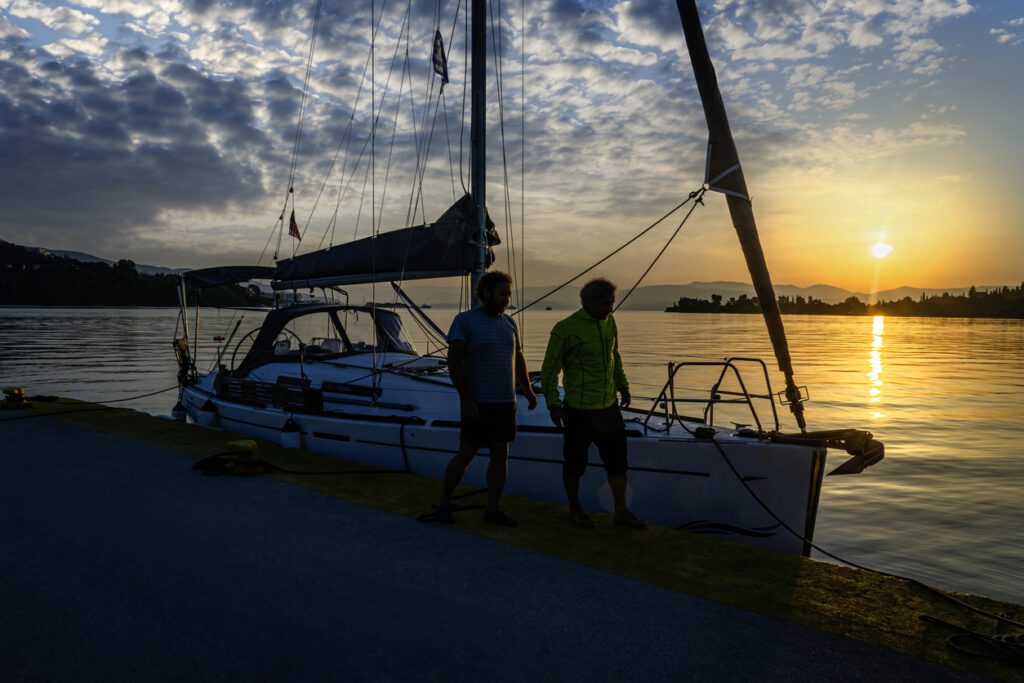 Two men stand next to their boat at sunrise in Corfu island, Greece.